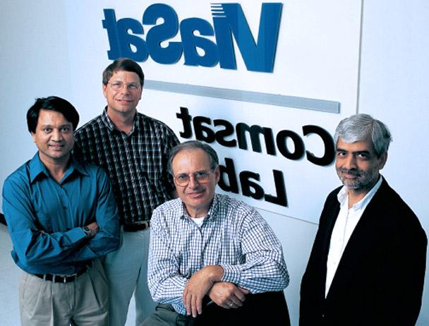 在Viasat Comsat实验室的标识前，四名Viasat员工对着摄像机微笑